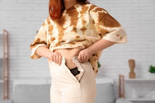 Image of woman trying to do her trousers up after pregnancy weight gain Hythe